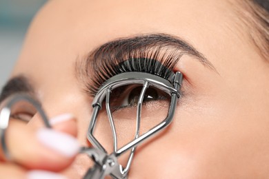 Young woman using eyelash curler on grey background, closeup