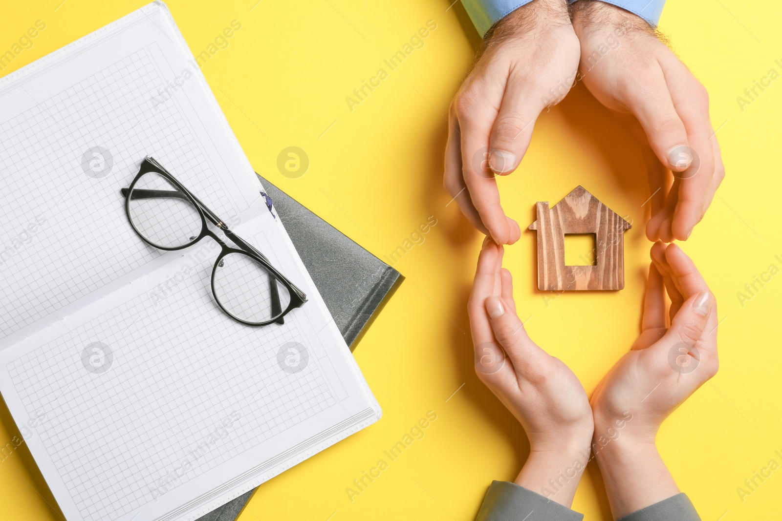 Photo of Couple holding hands near figure of house on color background, top view. Home insurance