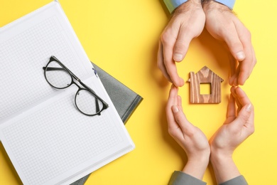 Photo of Couple holding hands near figure of house on color background, top view. Home insurance