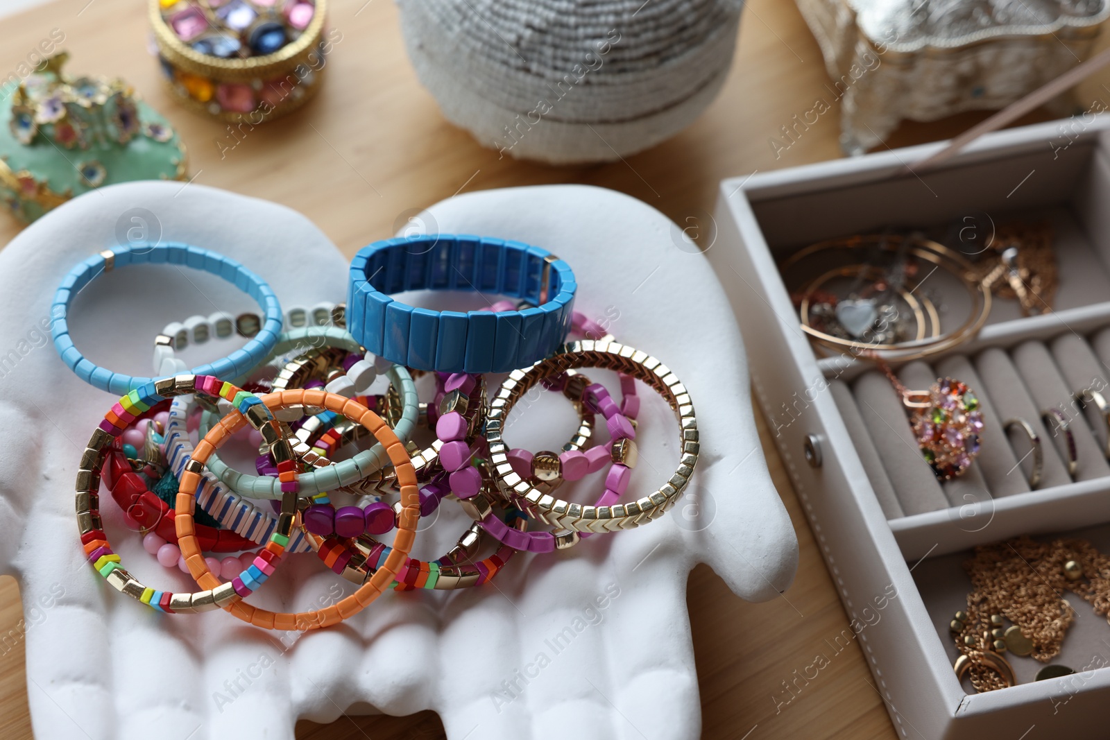 Photo of Ceramic hand stand with many stylish bracelets and jewelry boxes on wooden table, closeup