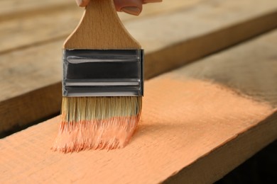 Woman painting wooden surface with coral dye, closeup