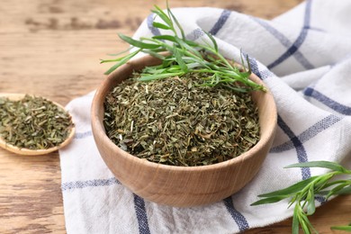 Dry and fresh tarragon in bowl on wooden table, closeup