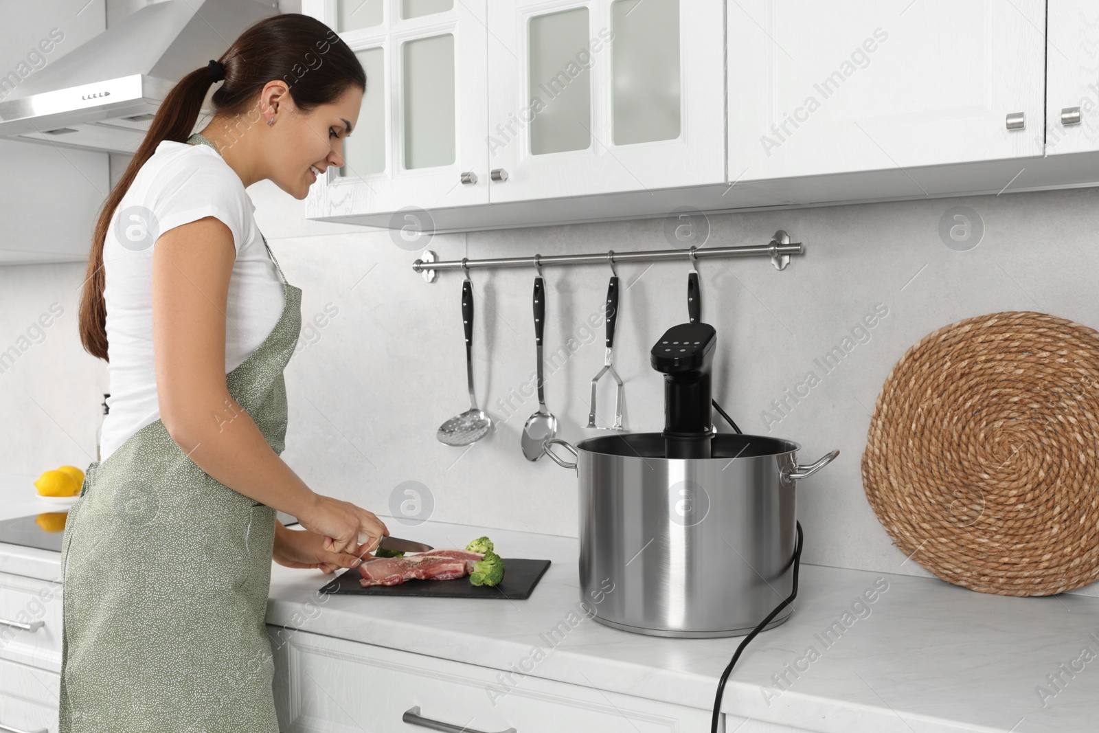 Photo of Woman cutting meat near pot with sous vide cooker in kitchen. Thermal immersion circulator