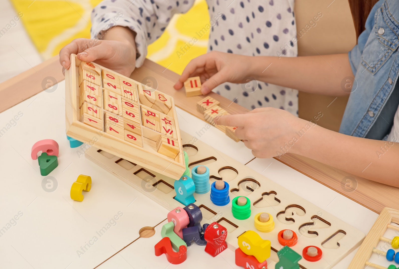 Photo of Mother and daughter playing with different math game kits at desk, closeup. Study mathematics with pleasure