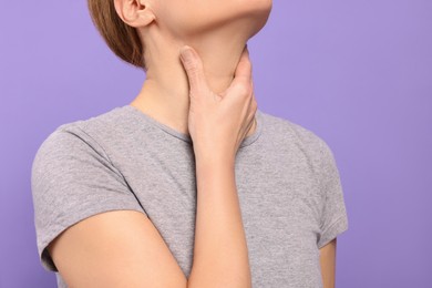Photo of Woman suffering from sore throat on violet background, closeup