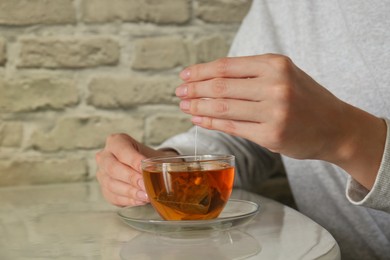 Photo of Woman taking tea bag out of cup at table indoors, closeup