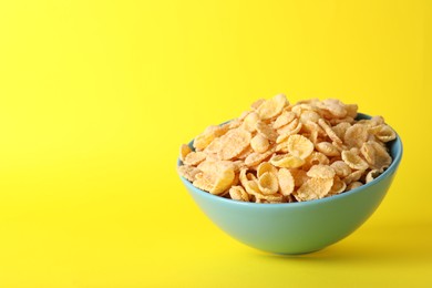 Photo of Bowl of tasty crispy corn flakes on yellow background, space for text