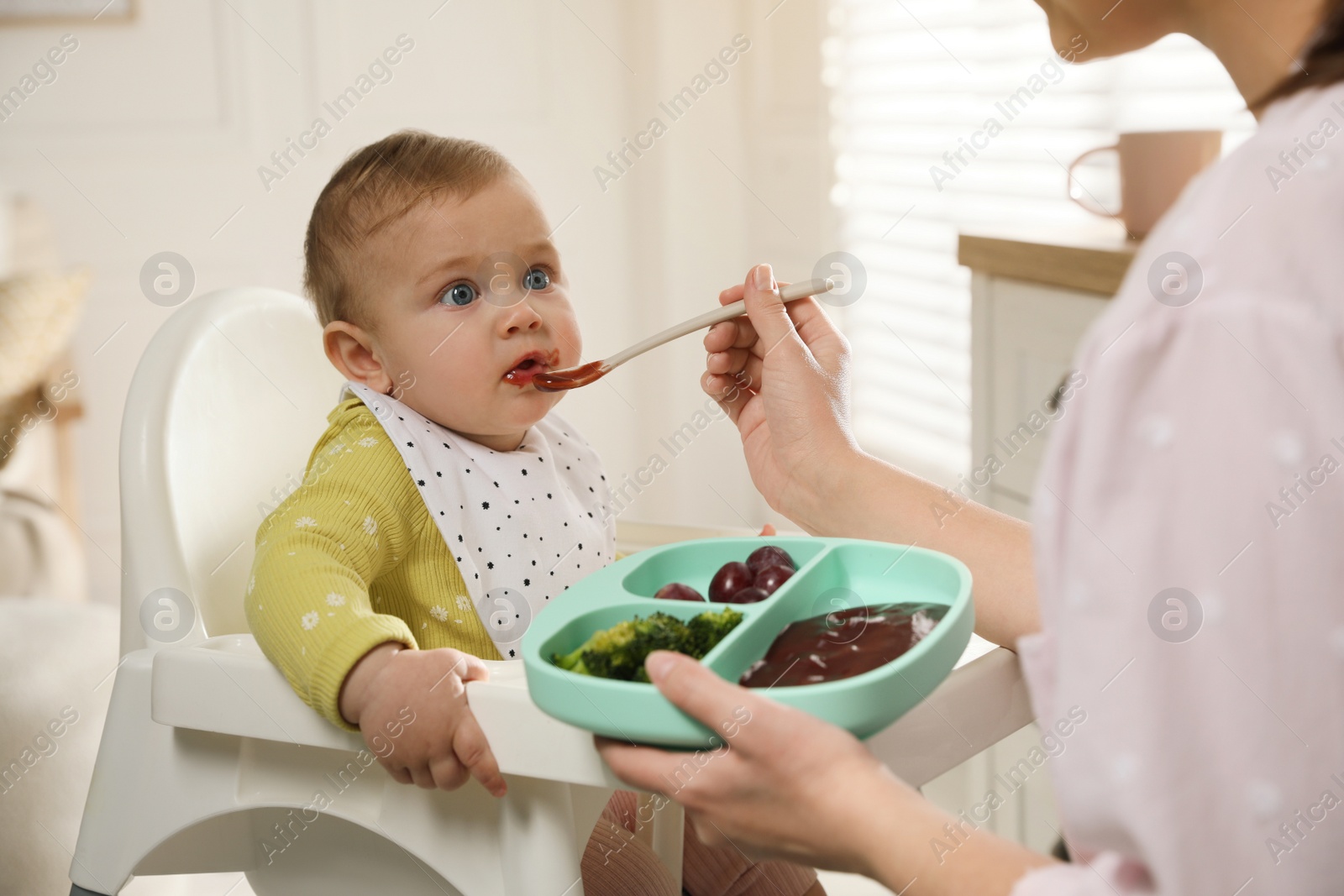 Photo of Mother feeding her little baby at home. Kid wearing bib