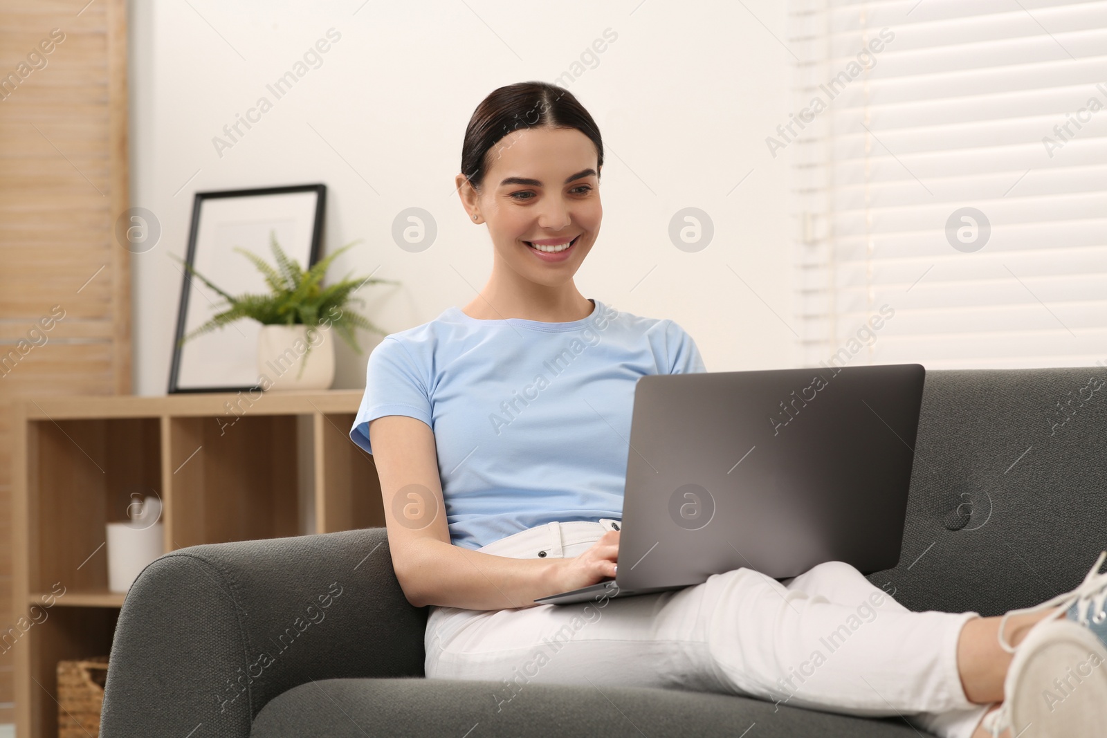 Photo of Happy woman working with laptop on sofa at home