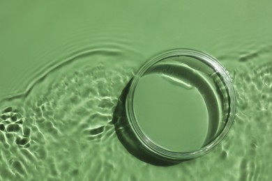 Photo of Stylish presentation for product. Glass podium in water on pale green background, top view. Space for text