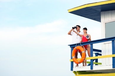 Photo of Lifeguards with megaphone and binocular on watch tower against blue sky