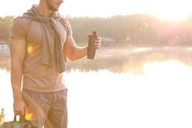 Photo of Young man drinking water on shore of beautiful lake. Camping season