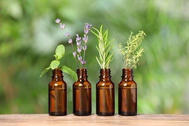 Photo of Bottles with essential oils and plants on wooden table against blurred green background