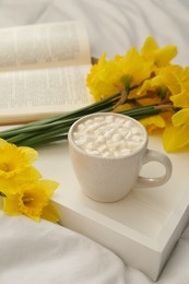 Beautiful daffodils and cup of hot drink on bed