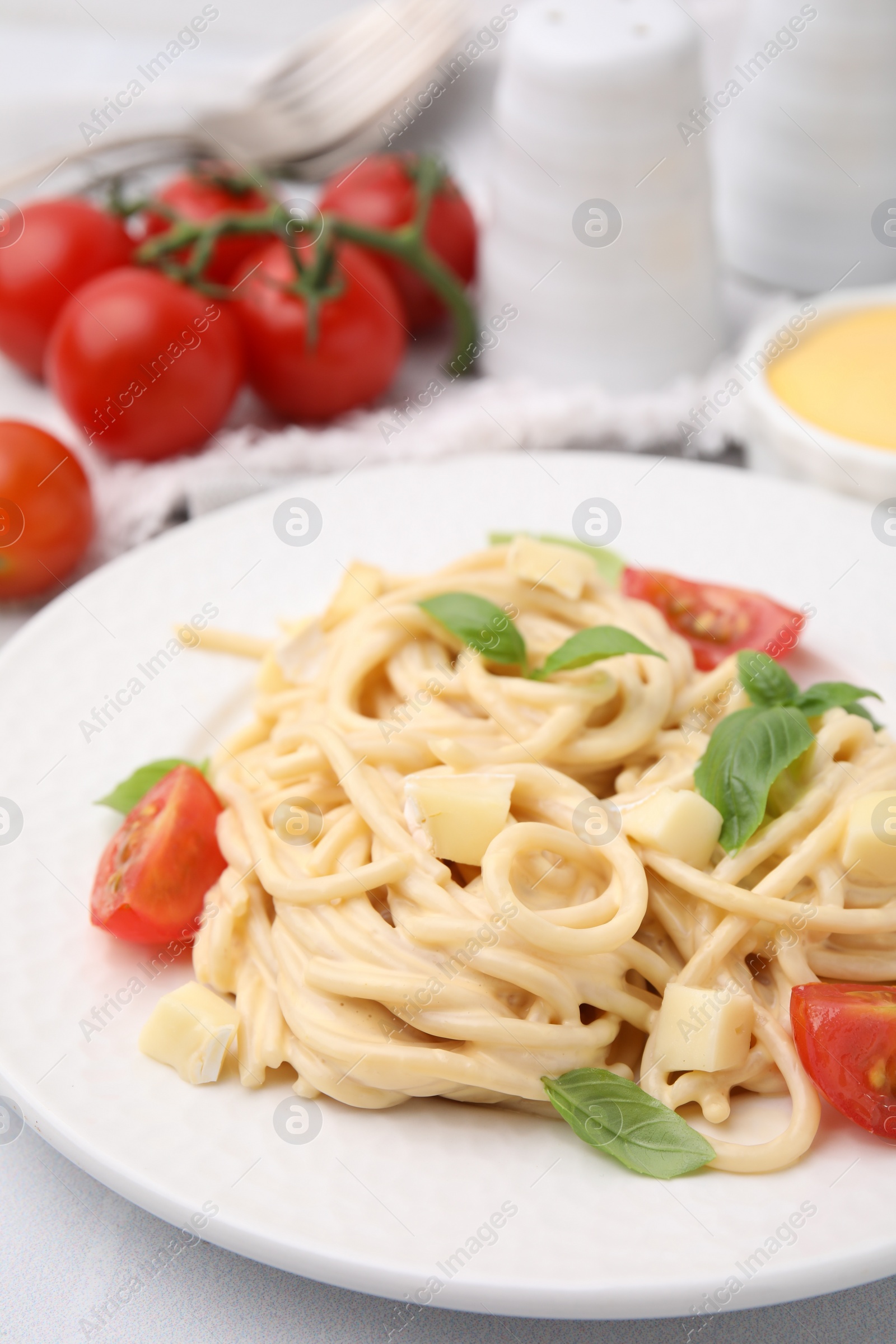 Photo of Delicious pasta with brie cheese, tomatoes and basil leaves on white table, closeup