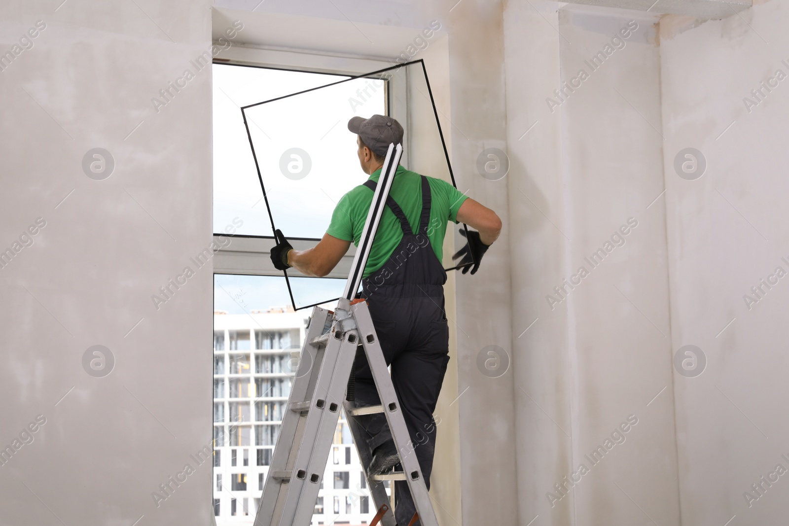 Photo of Worker on folding ladder installing window indoors, back view