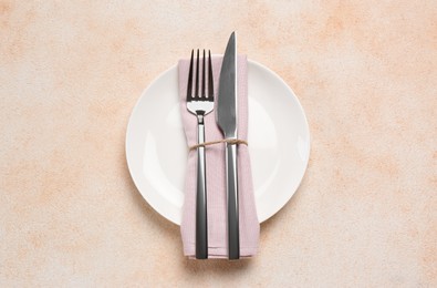 Plate, fork and knife on beige table, top view