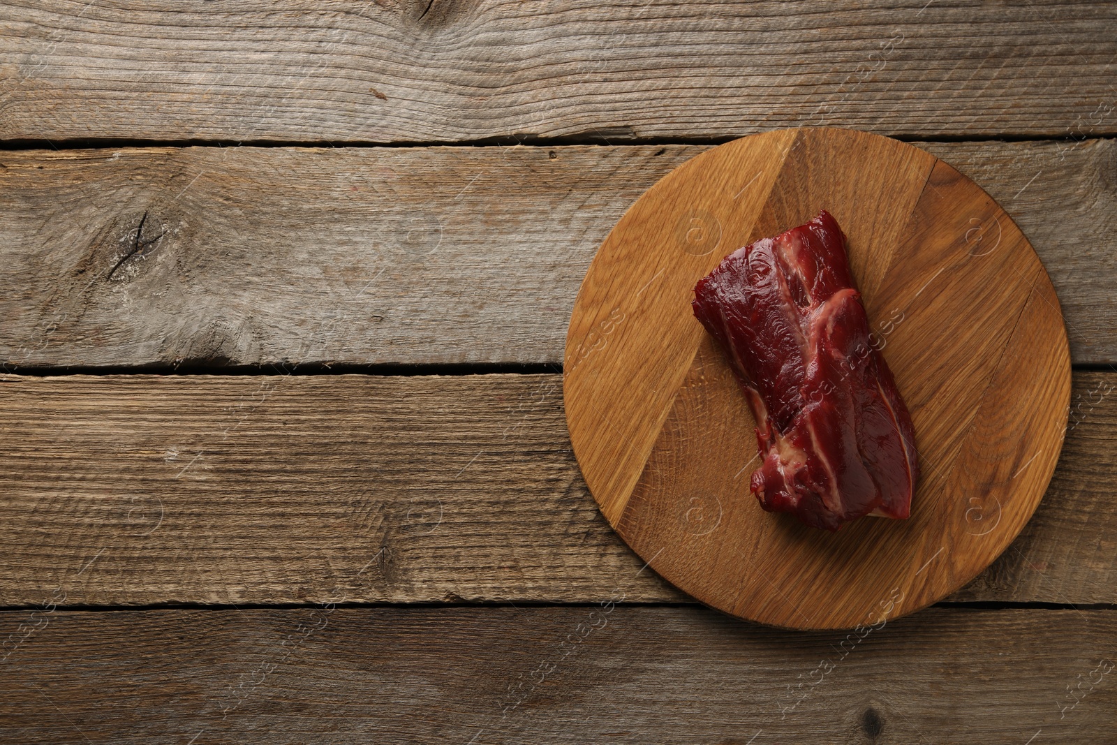Photo of Piece of raw beef meat on wooden table, top view. Space for text