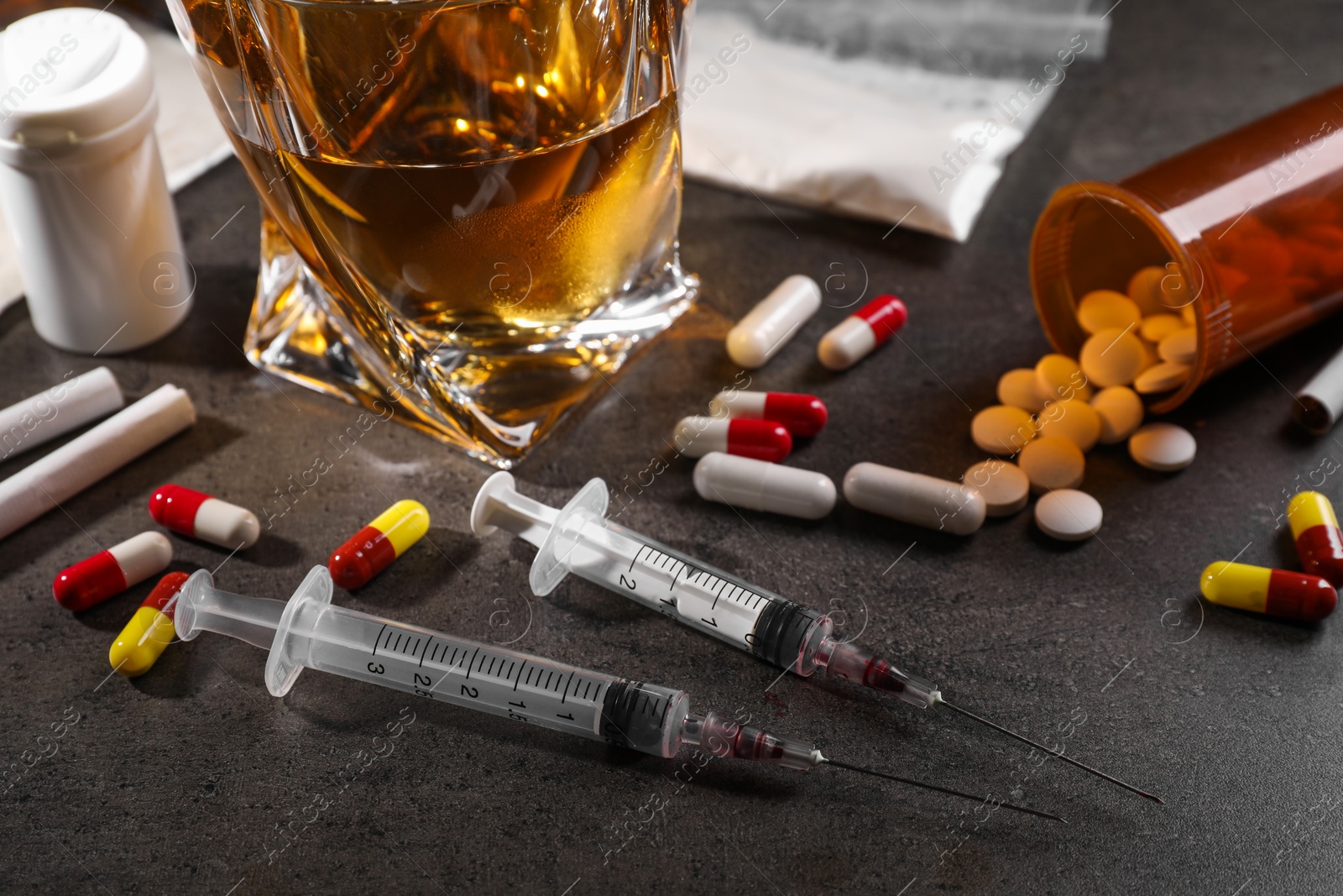 Photo of Alcohol and drug addiction. Whiskey in glass, syringes, pills and cigarettes on grey table, closeup