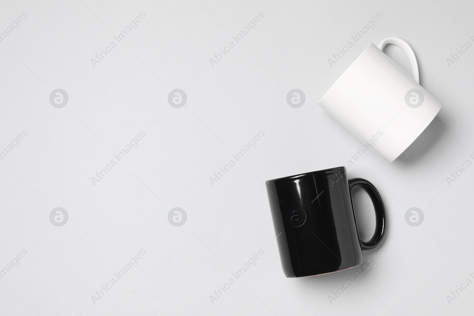 Black and white ceramic mugs on light background, flat lay. Space for text Photo of Black and white ceramic mugs on light background, flat lay. Space for text