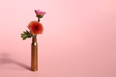 Photo of Bullet cartridge case and beautiful chrysanthemum flowers on pink background, space for text