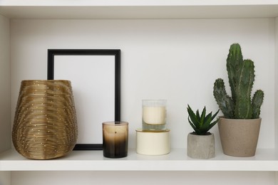 Beautiful houseplants, scented candles, frame and vase on shelf