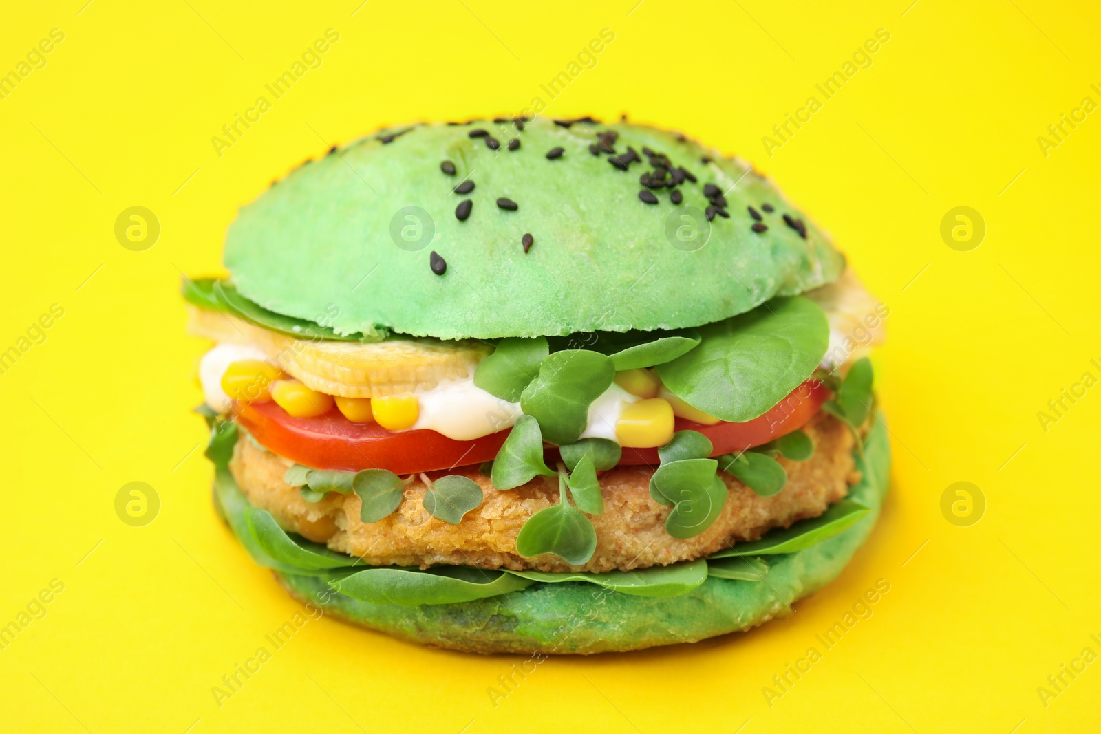 Photo of Tasty green vegan burger with vegetables, patty and microgreens on yellow background, closeup