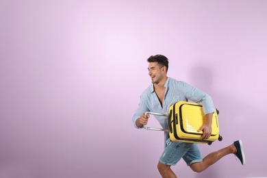Photo of Young man running with suitcase on color background. Space for text