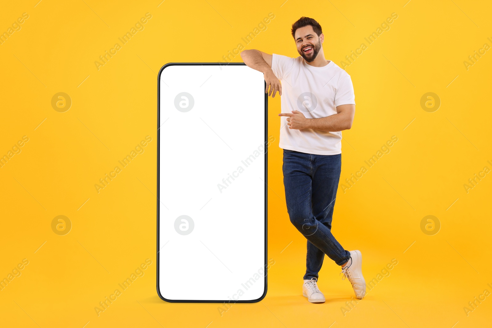 Image of Man pointing at huge mobile phone with empty screen on dark beige background. Mockup for design