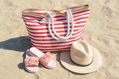 Stylish striped bag with straw hat and slippers on sandy beach