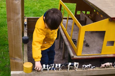 Photo of Little boy playing with toy cows in park