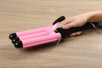 Woman holding modern triple curling iron on wooden background, closeup