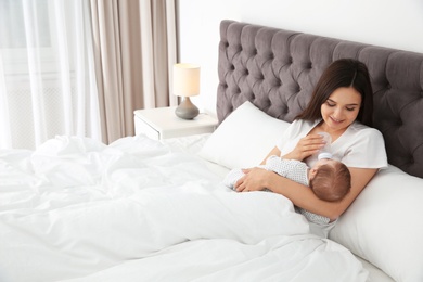 Photo of Woman feeding her baby from bottle on bed. Space for text