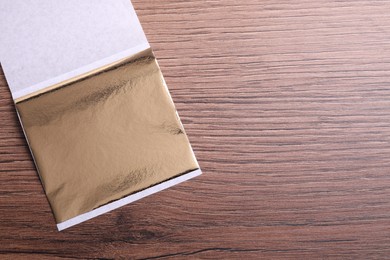 Photo of Edible gold leaf sheet on wooden table, top view. Space for text