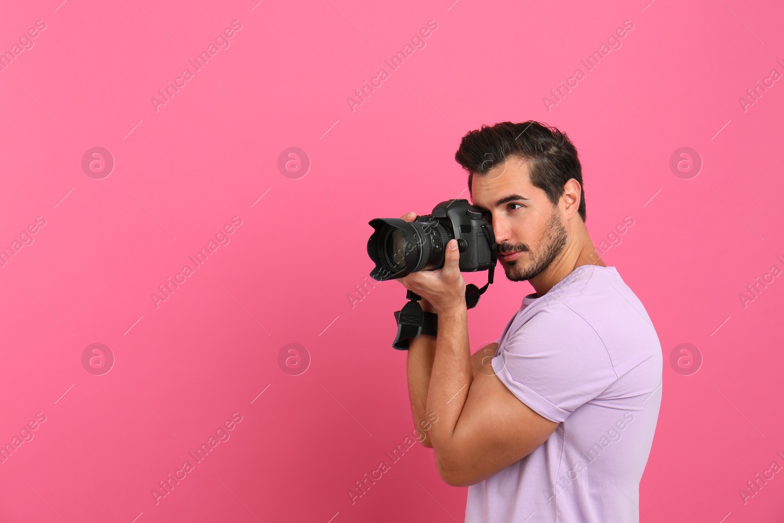 Photo of Young professional photographer taking picture on pink background. Space for text