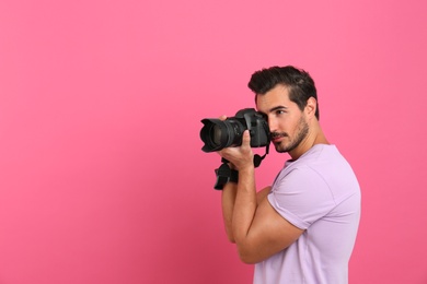 Young professional photographer taking picture on pink background. Space for text
