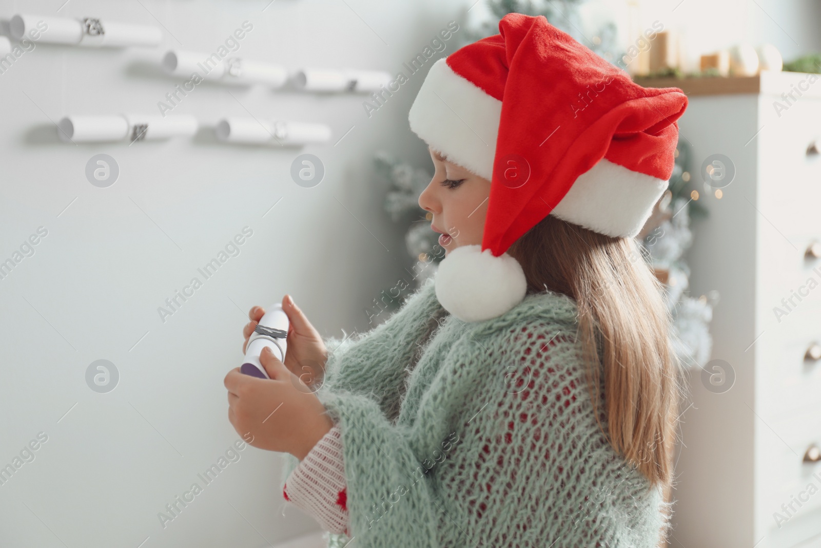 Photo of Cute little girl in Santa hat holding gift from New Year advent calendar at home