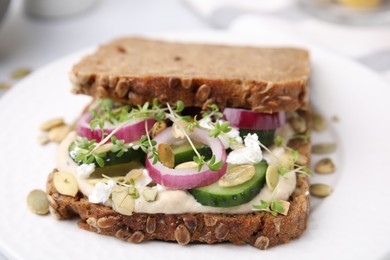 Tasty vegan sandwich with cucumber, onion, hummus and pumpkin seeds on plate, closeup