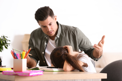 Photo of Father scolding his daughter while helping with homework at table indoors