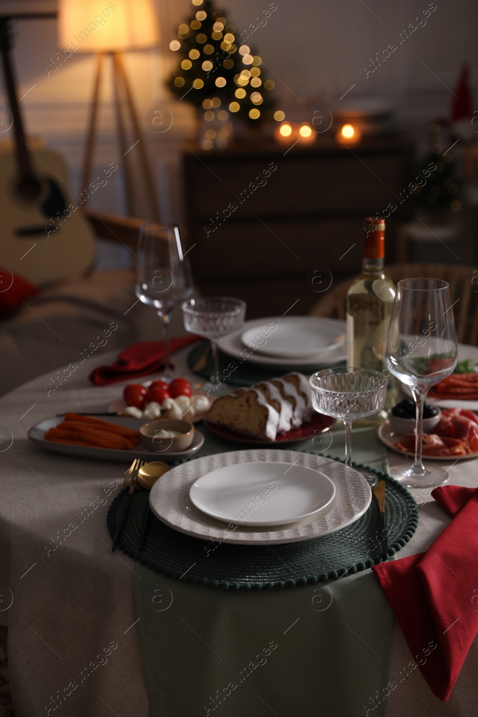 Photo of Christmas table setting with bottle of wine, appetizers and dishware indoors