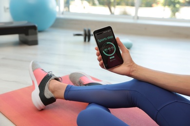 Young woman using fitness app on smartphone indoors, closeup