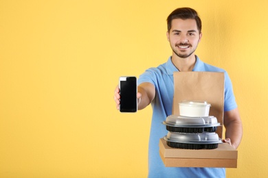 Photo of Young man holding orders and smartphone on color background, mockup for design. Online food delivery