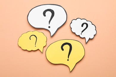 Photo of Paper speech bubbles with question marks on beige background, flat lay