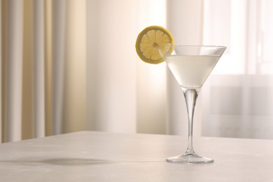Photo of Elegant martini glass with fresh cocktail and lemon slice on beige marble table indoors. Space for text