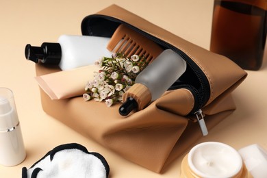 Photo of Preparation for spa. Compact toiletry bag with different cosmetic products and flowers on beige background, closeup