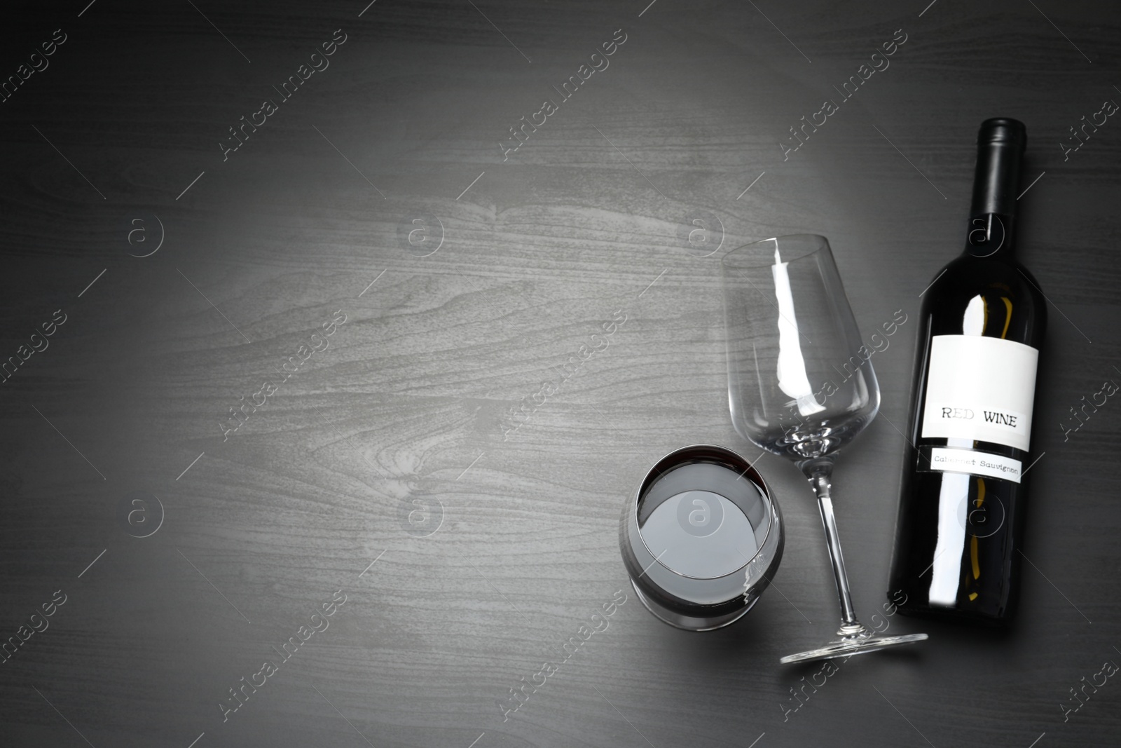 Photo of Glasses and bottle with red wine on dark background, flat lay. Space for text