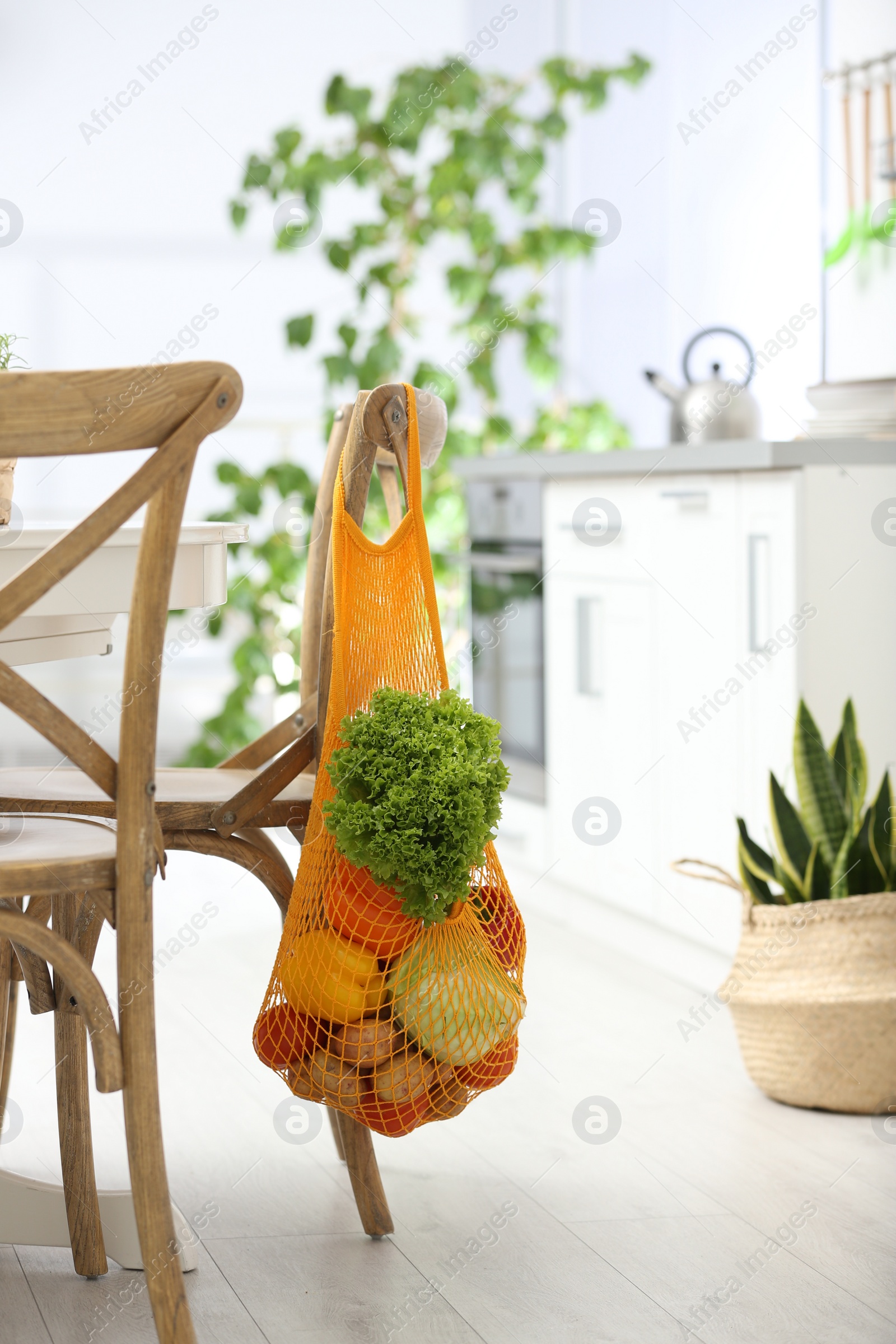 Photo of Net bag with vegetables hanging on wooden chair in kitchen