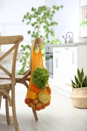 Net bag with vegetables hanging on wooden chair in kitchen