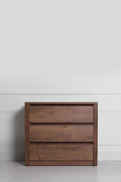 Wooden chest of drawers near white wall indoors, space for text