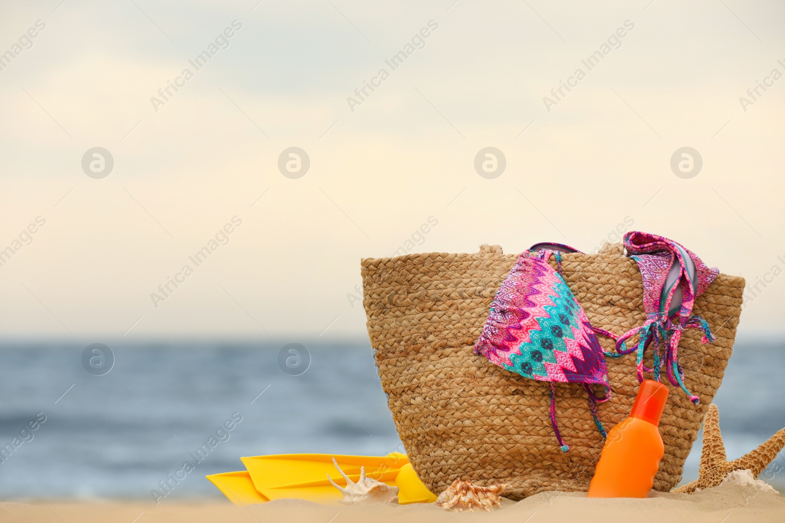 Photo of Bag and different beach objects on sand near sea, space for text